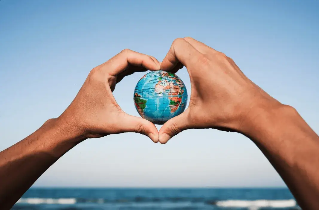 Hands forming heart shape around globe with ocean background, symbolizing love for Earth, sustainability, and global unity
