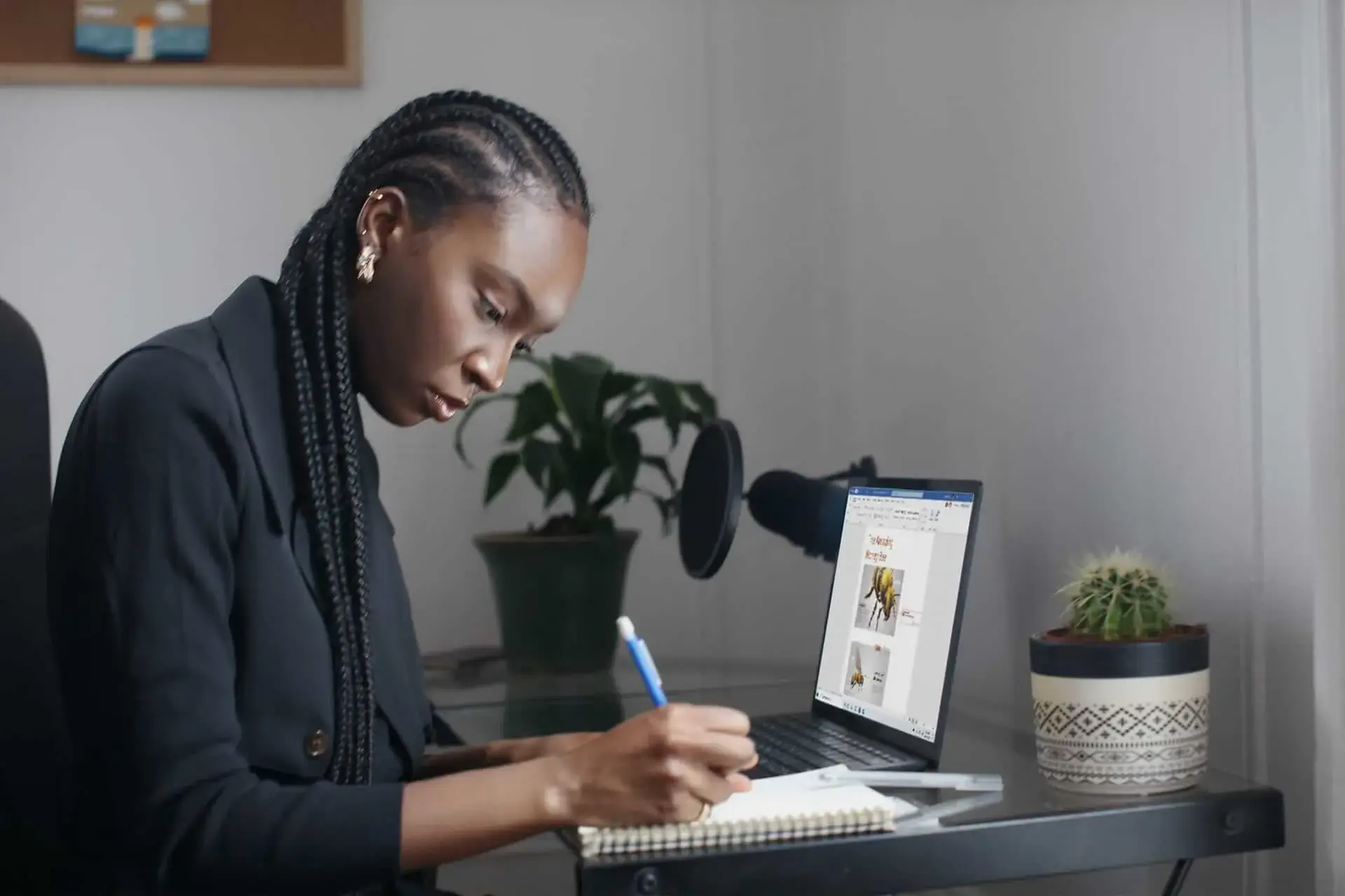 Woman taking notes while working on a presentation on her laptop in a home office setup.