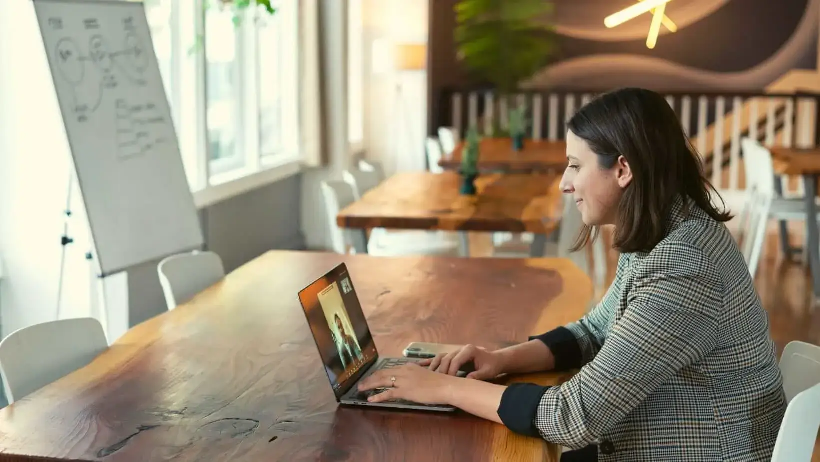 Woman attending a video call on a laptop in a stylish, well-lit workspace.