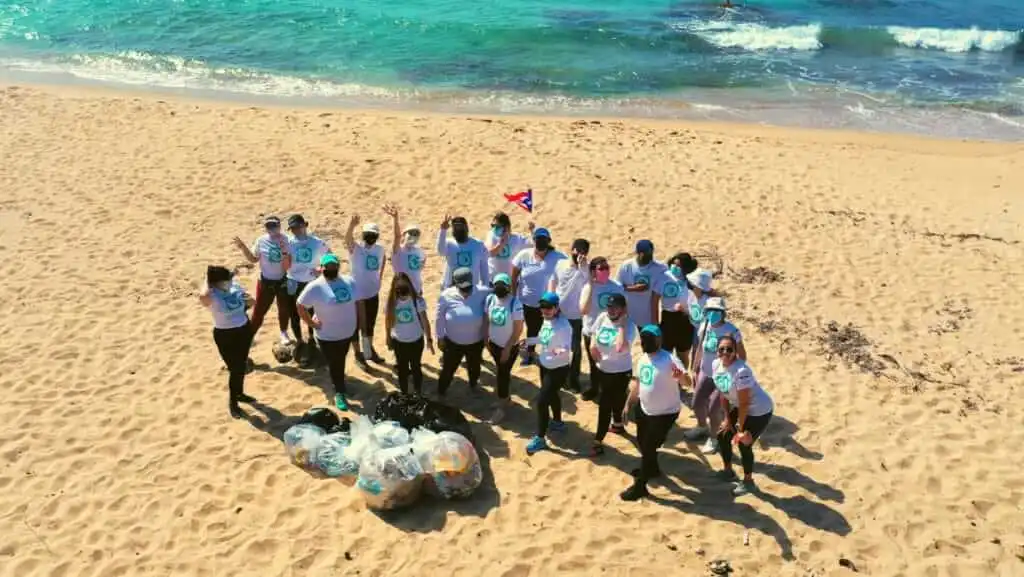 SPECTRAFORCE team members standing on the beach, collecting trash and working together to clean up the shoreline, demonstrating their community effort and resilience after Hurricane Maria.
