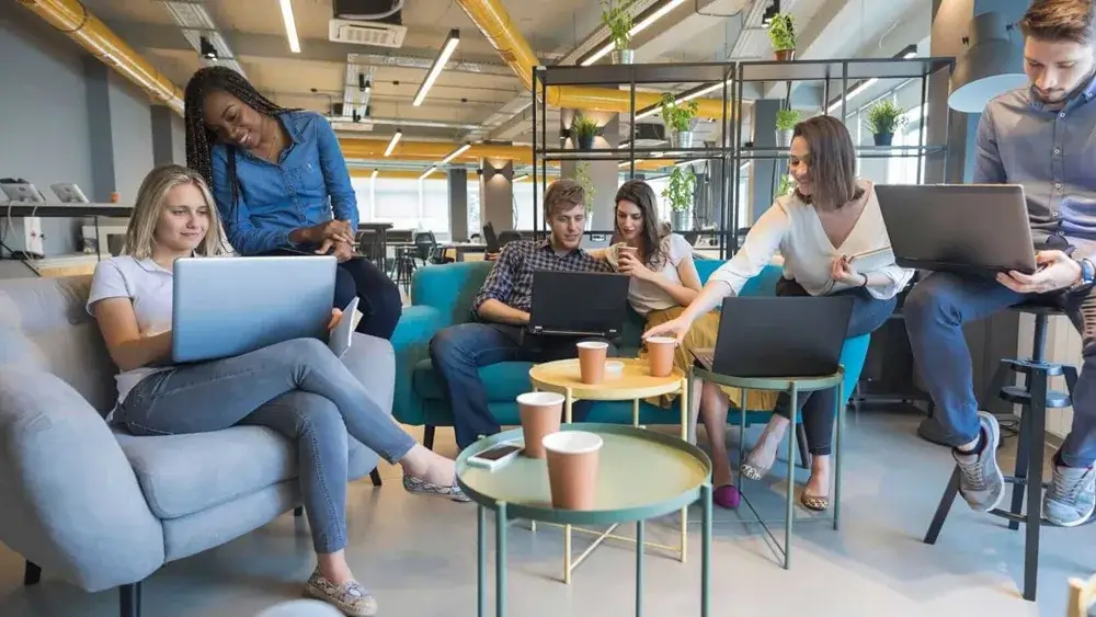 Group of young professionals collaborating with laptops in a colorful, open office workspace.