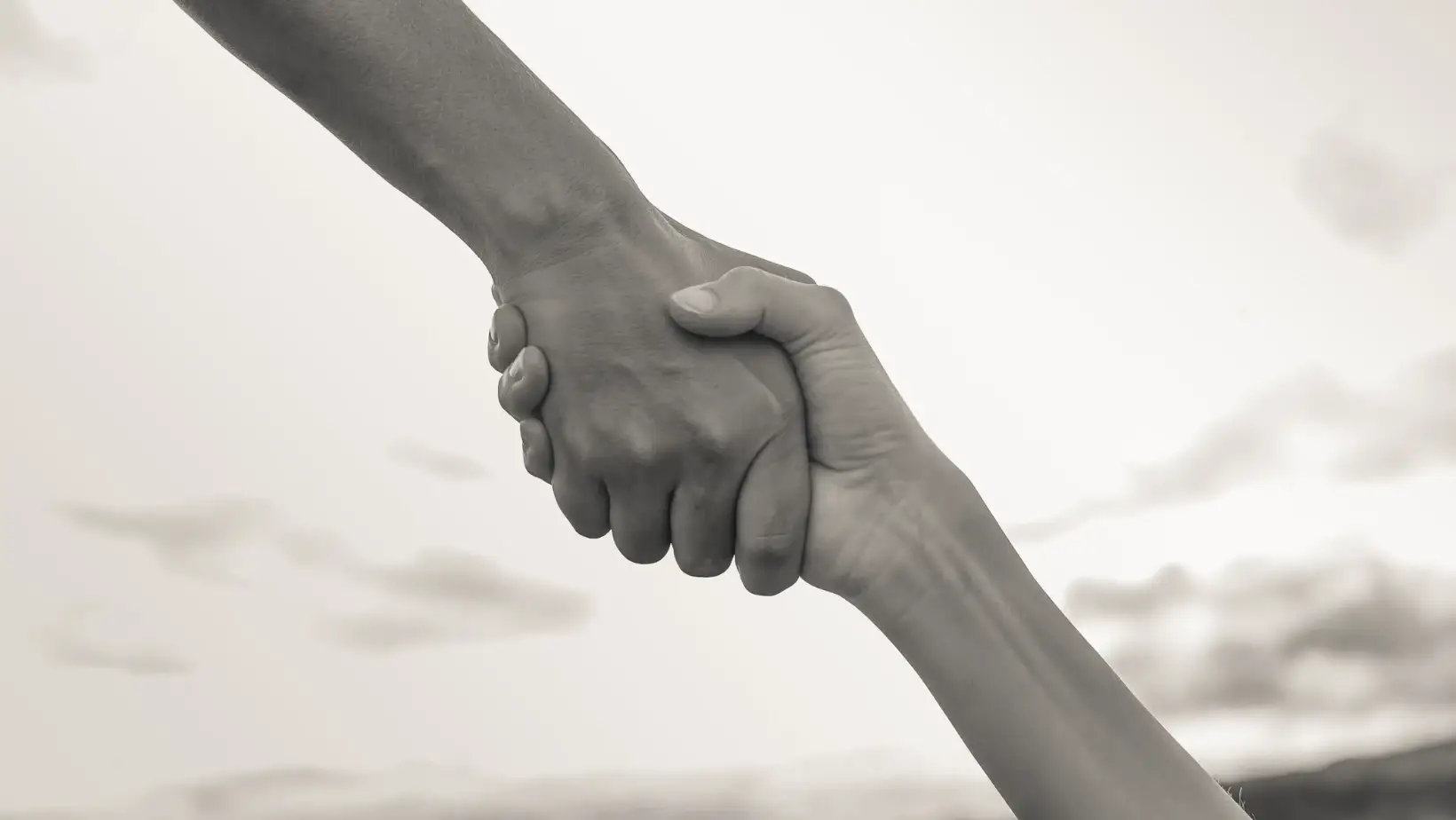 Two hands clasped in a firm grip against a blurred background, symbolizing connection, trust, and support.