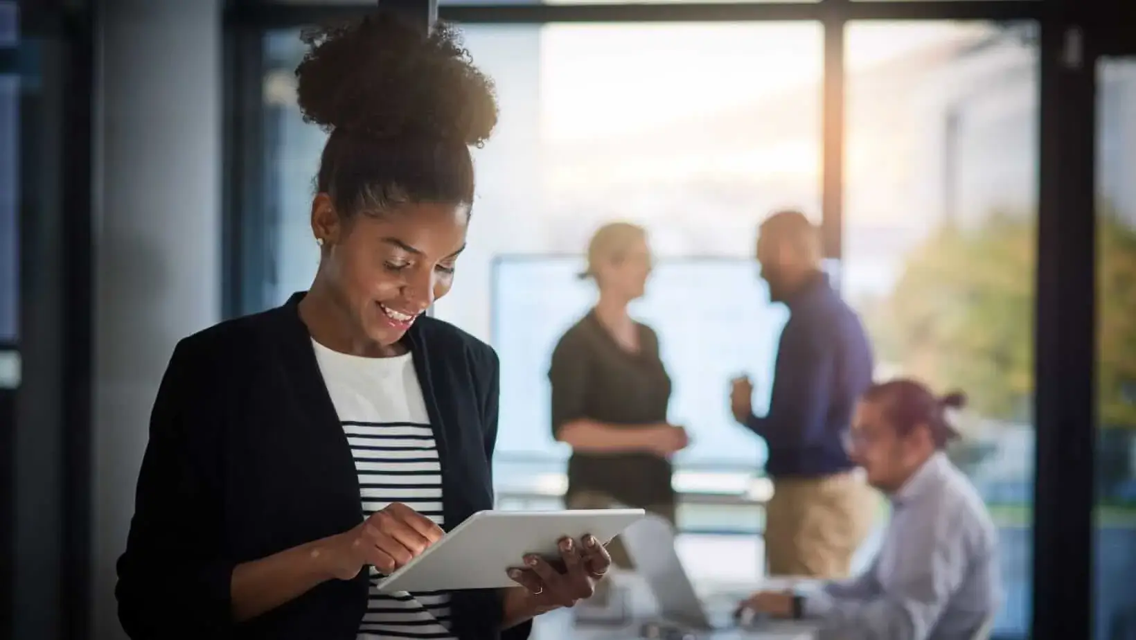 Confident professional using a tablet with a collaborative team in the background.