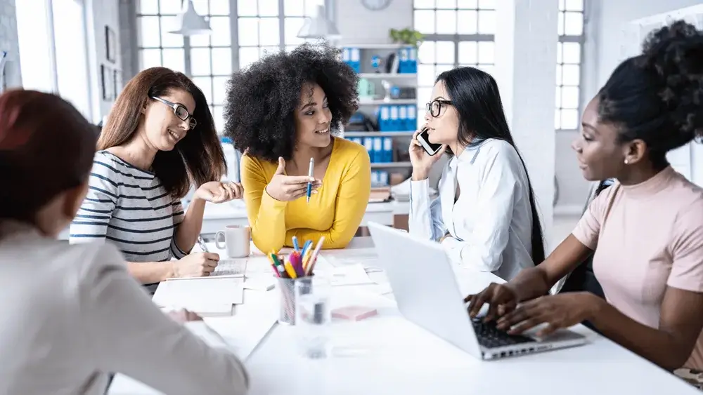 5 women discussing and taking notes sitting on a table