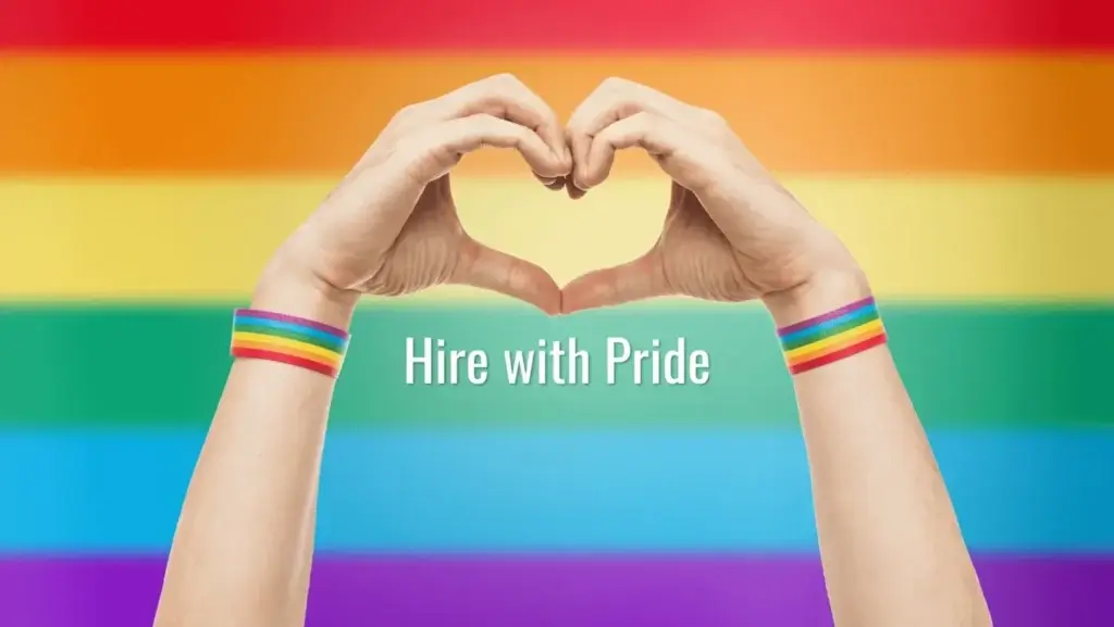 Hands forming a heart shape against a rainbow background, wearing pride wristbands, with the text “Hire with Pride.”