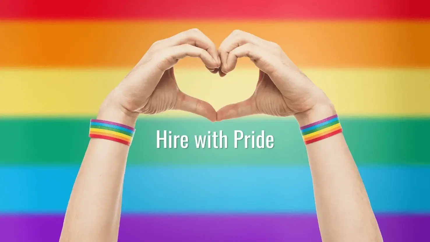 Hands forming a heart shape against a rainbow background, wearing pride wristbands, with the text “Hire with Pride.”