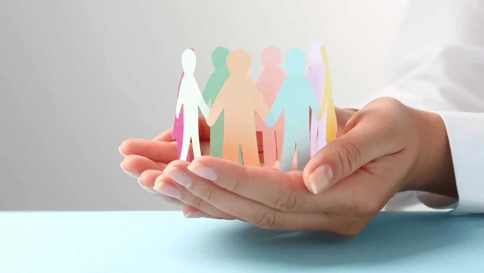 Hands holding a circle of colorful paper cutout people, representing unity, diversity, and community support