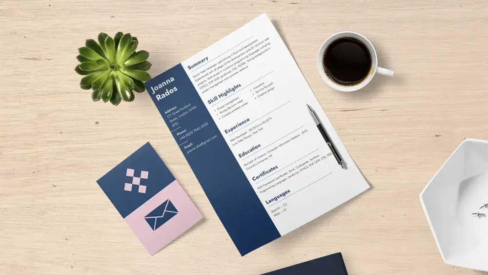 Flat lay of a resume on desk with coffee, plant, business card, pen, and office supplies