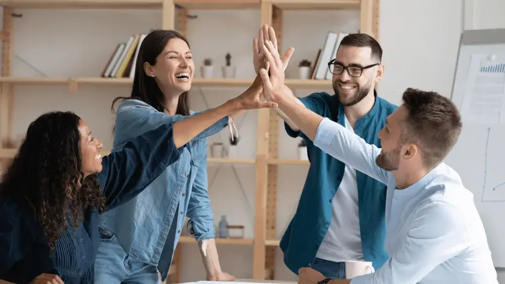 Diverse team celebrating success with high-fives, promoting inclusive workplace culture and employee collaboration.