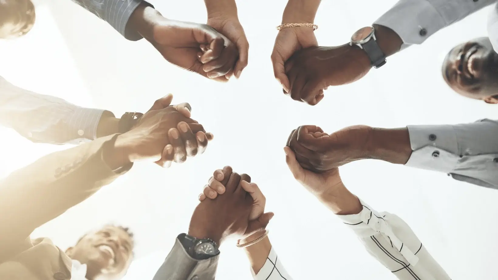 Diverse team holding hands in unity, symbolizing teamwork, inclusion, collaboration, and workplace diversity from a low angle view