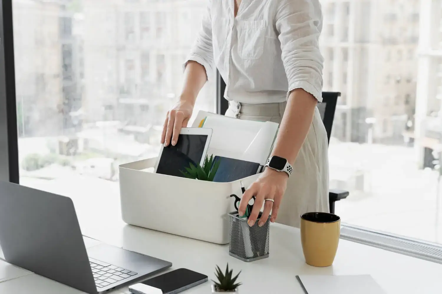 Person packing office items into a box, indicating resignation or last day at work in modern office