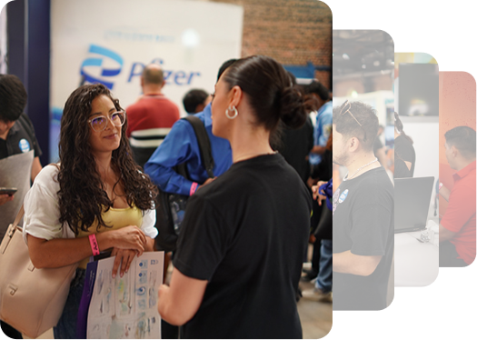Two women engage in conversation at an event, surrounded by attendees and booths in a lively atmosphere.