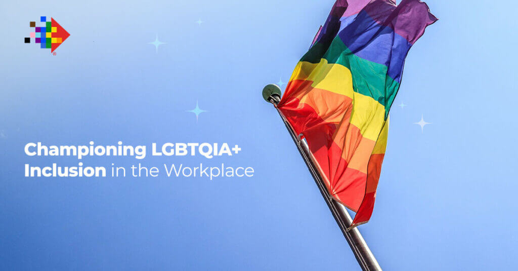 A rainbow flag waves on a flagpole against a clear blue sky. Text on the image reads, "Championing LGBTQIA+ Inclusion in the Workplace." There's a colorful, pixelated logo in the top left corner, symbolizing our commitment to fostering inclusion in the workplace.