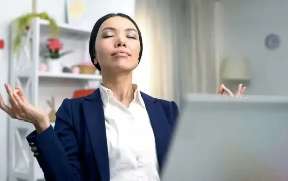 Person in a blue blazer sitting calmly with hands raised in a cozy, modern workspace, reflecting anxiety relief practices.