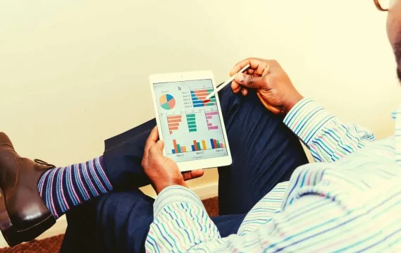 Man analyzing colorful graphs and charts on a tablet using a stylus, dressed in business attire.