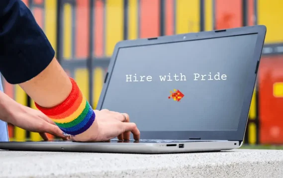 Person typing on laptop wearing rainbow pride wristband, with screen displaying “Hire with Pride” and Spectraforce logo.