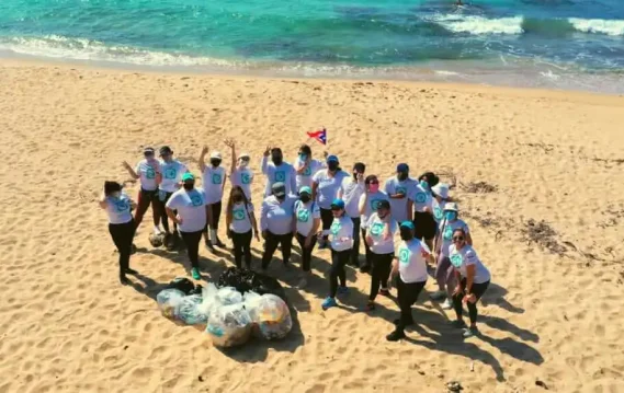 SPECTRAFORCE team members standing on the beach, collecting trash and working together to clean up the shoreline, demonstrating their community effort and resilience after Hurricane Maria.