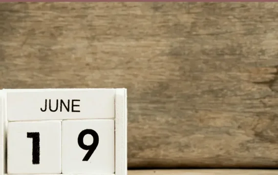 A wooden block calendar displays the date "June 19" against a rustic wooden background.