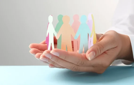 Diseno-sin-titulo Hands holding a circle of colorful paper cutout people, representing unity, diversity, and community support