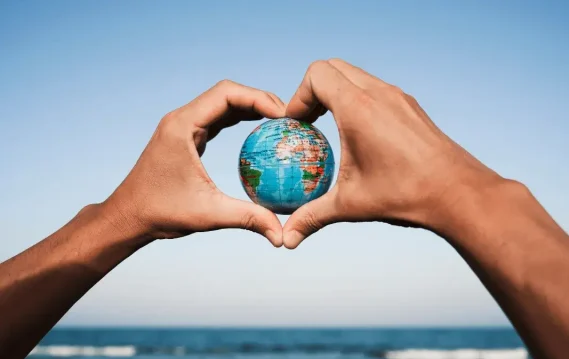 Hands forming heart shape around globe with ocean background, symbolizing love for Earth, sustainability, and global unity