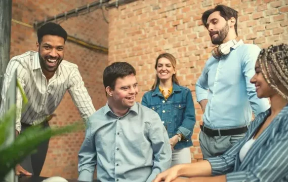 Inclusive team of coworkers, including a person with Down syndrome, laughing and collaborating in a modern workspace.