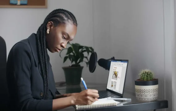 Hybrid-Schedule-Header-surface-yn9rw5s0PNE-resized Woman taking notes while working on a presentation on her laptop in a home office setup.