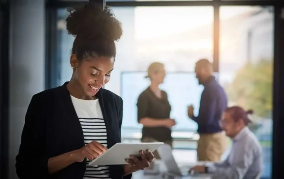 Productivity-Header Confident professional using a tablet with a collaborative team in the background.