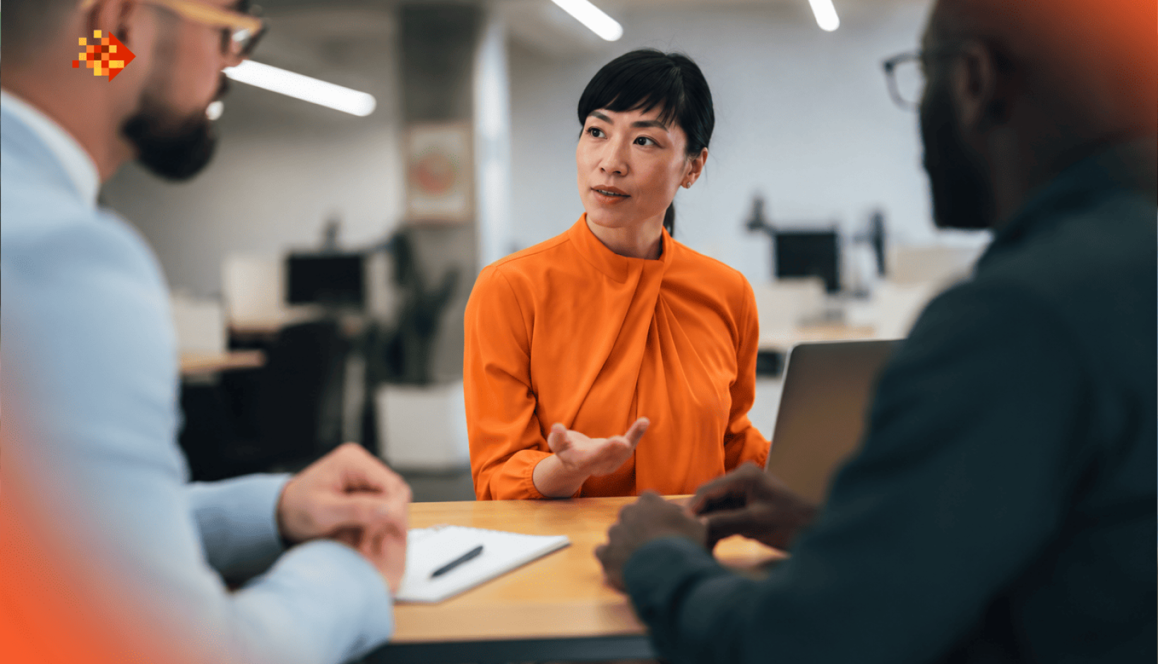 Three professionals discussing recruitment strategy in a modern office, with a woman speaking across a conference table.