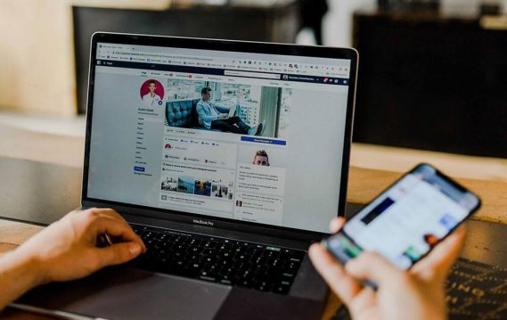A person surfing on social media on a laptop with a mobile device in hand