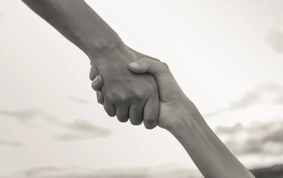 Two hands clasped in a firm grip against a blurred background, symbolizing connection, trust, and support.