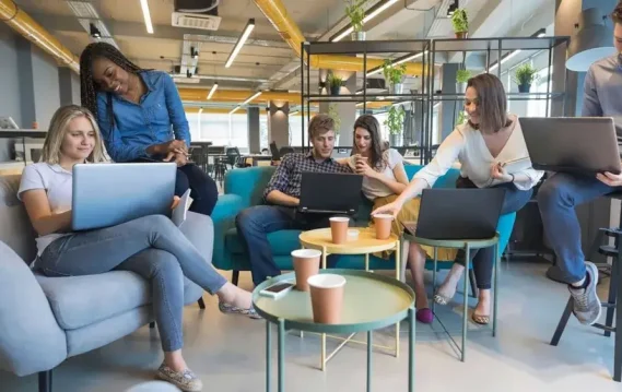 Group of young professionals collaborating with laptops in a colorful, open office workspace.