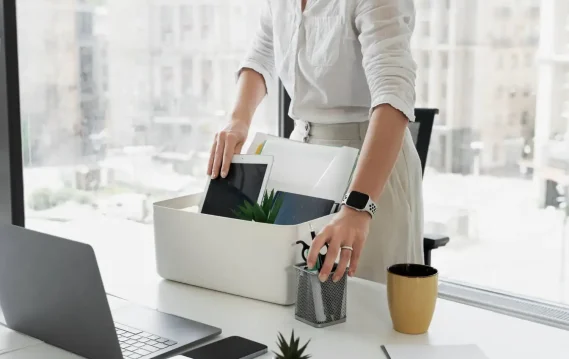 Person packing office items into a box, indicating resignation or last day at work in modern office